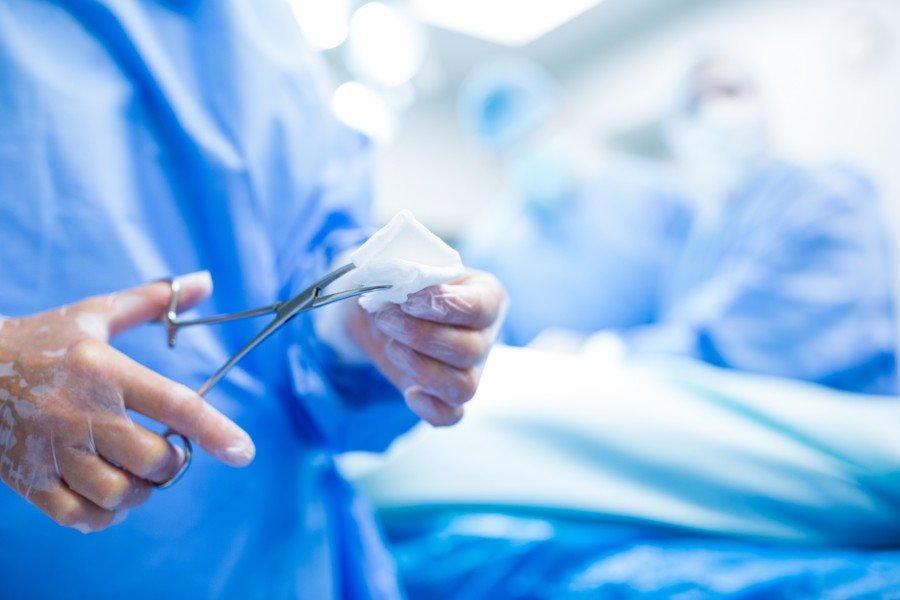 Surgeon in blue scrubs using surgical scissors to cut sterile gauze in an operating room.
