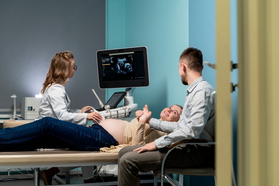 Antenatal Care consultation with a pregnant woman undergoing an ultrasound examination while her partner and healthcare provider are present.