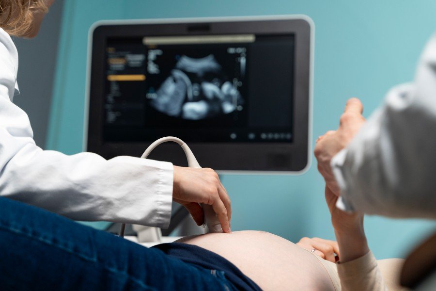 Pregnant woman receiving an ultrasound examination from a healthcare professional, with an ultrasound image visible on the monitor.