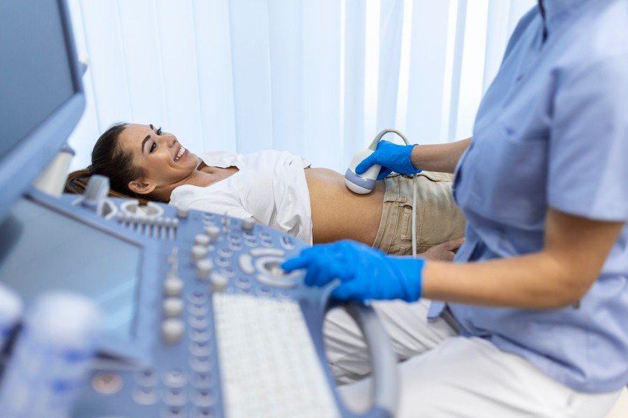 Obstetrician performing an ultrasound examination on a smiling pregnant woman in a clinic